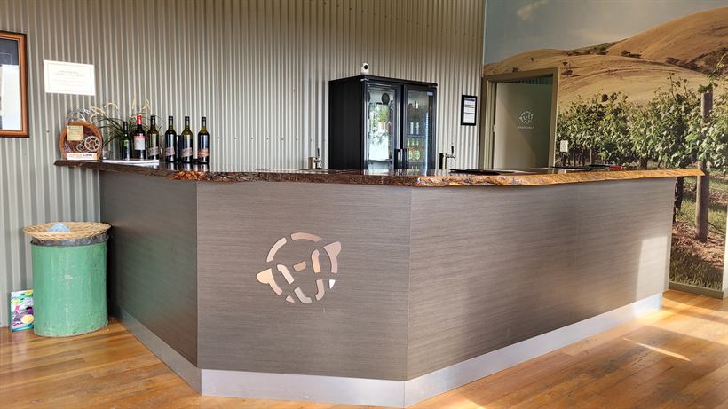 Tasting bar with the cut-steel logo on the front and wine bottles behind