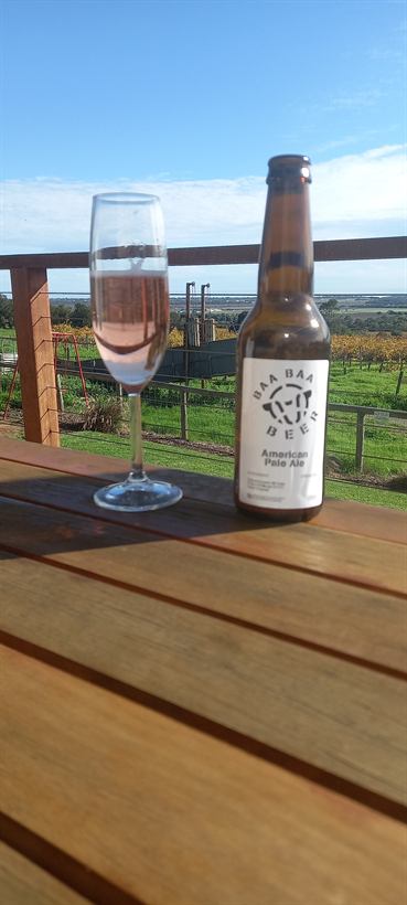 Glass of sparkling and a bottle of Baa Baa beer on the deck rail overlooking the vines