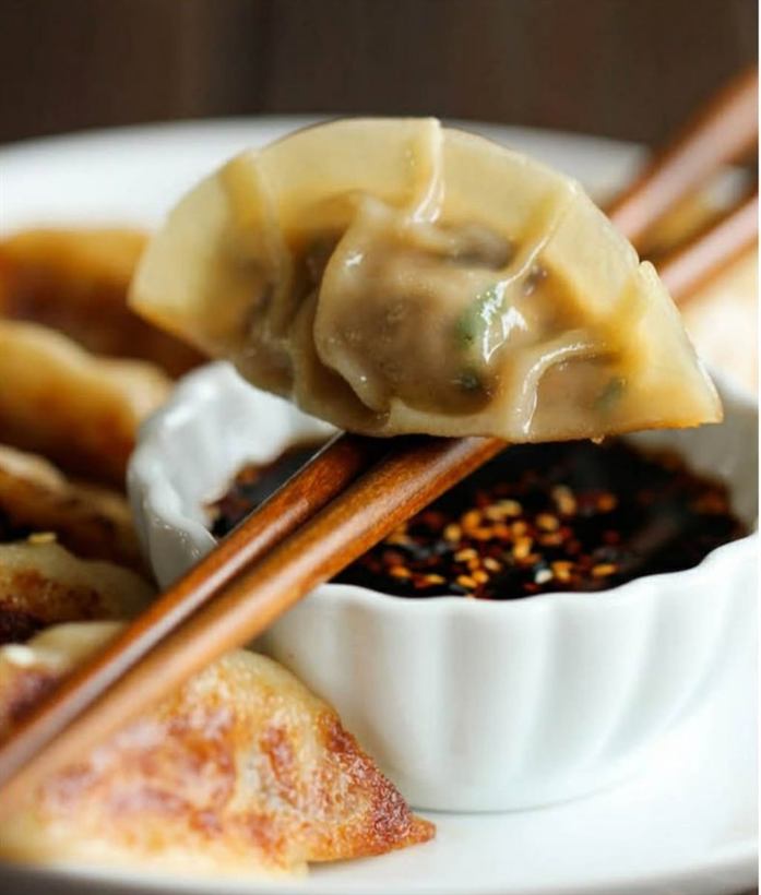 A dumpling held in chopsticks over chilli oil