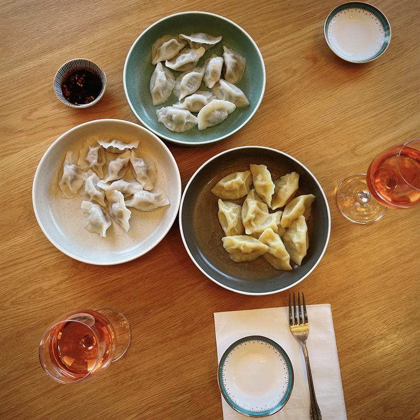 Three plates of dumplings, chilli oil and rosé on a timber table