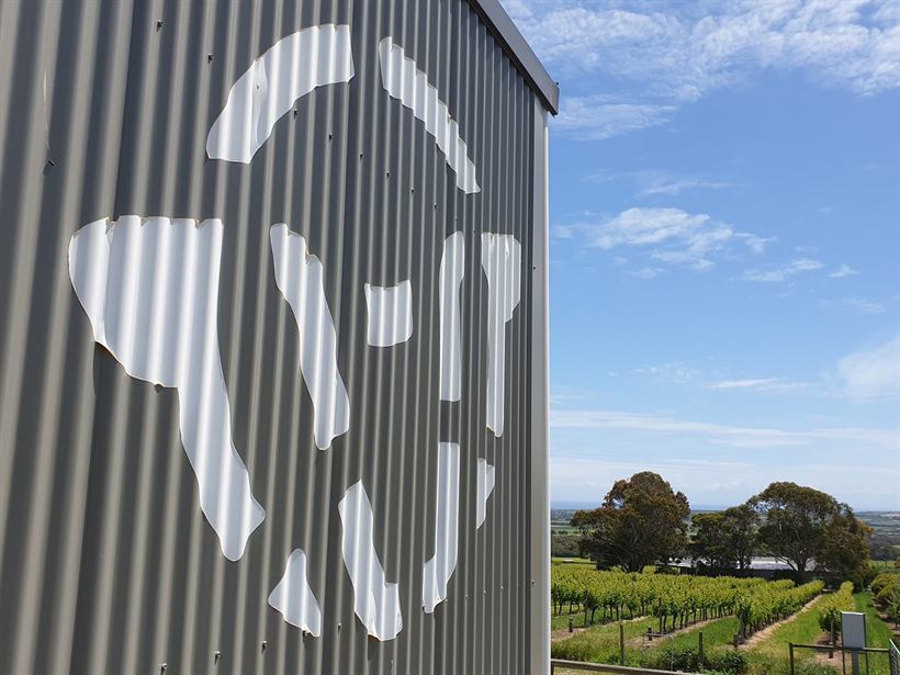 The estate sheep-face logo cut into corrugated steel with vines behind